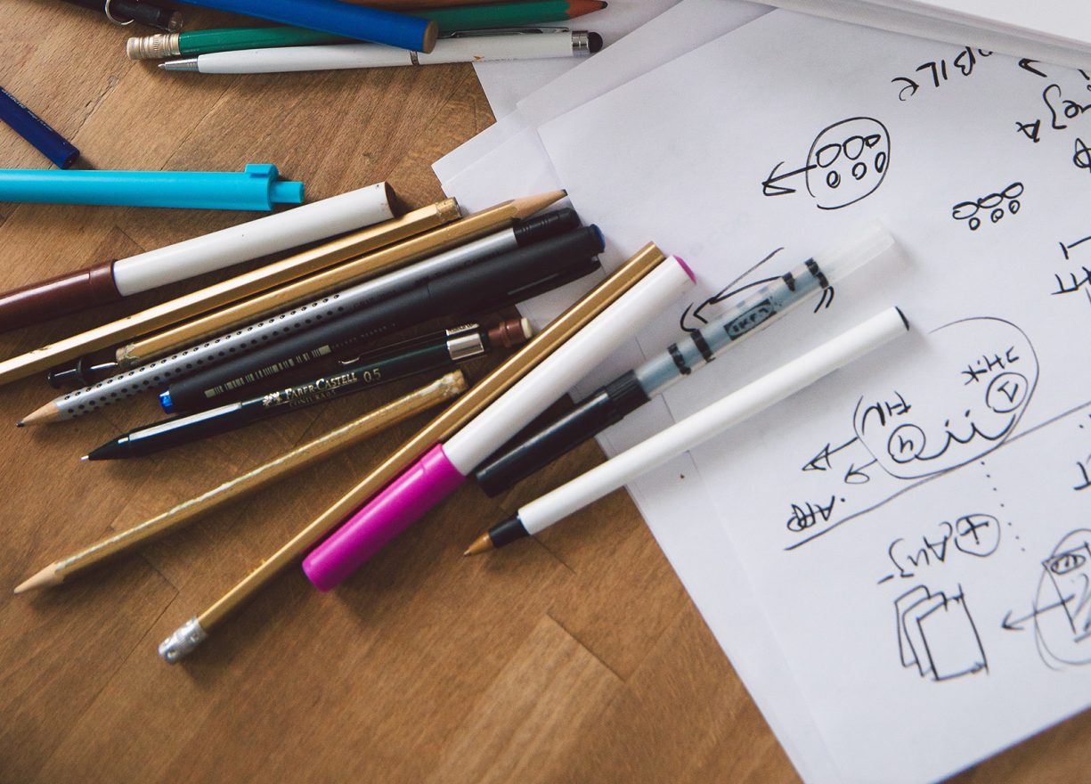 various types of pens scattered on desk with notes made on paper